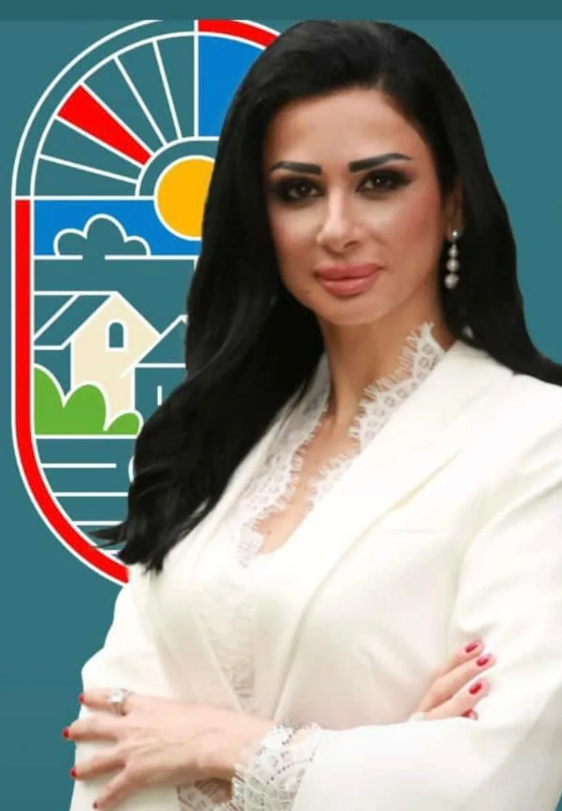ميرنا نكد بسترة بيضاء، مكتوفة الذراعين.