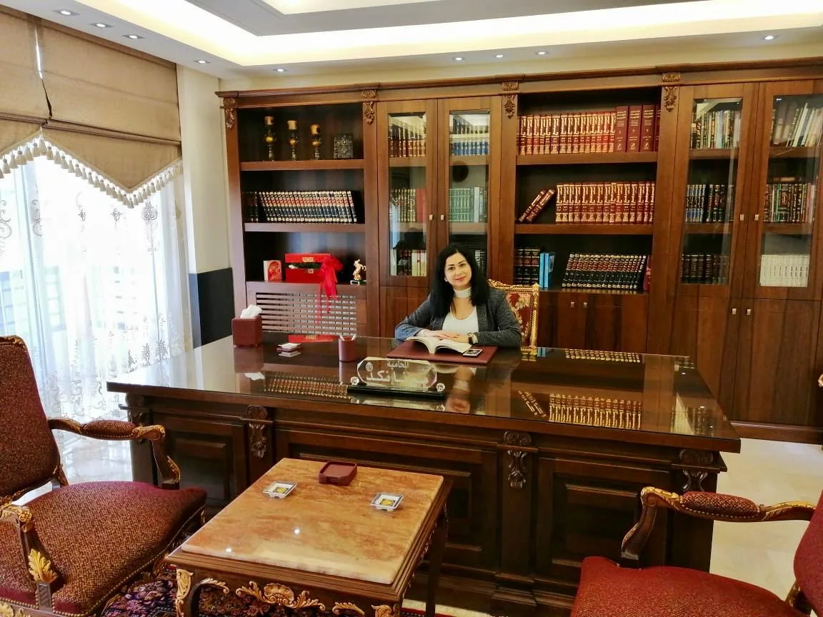 المكتب: ميرنا نكد إلى مكتبها، ورفوف المجلدات القانونية خلفها.